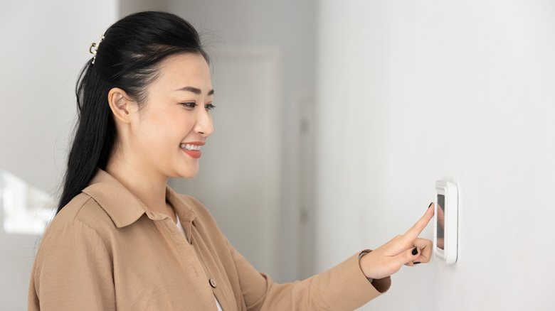 Smiling woman adjusts thermostat controls