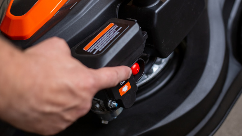 Person's hand pointing at the red primer bulb on a lawn mower