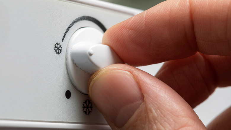 A close-up image of a person's hand adjusting temperature dial on fridge