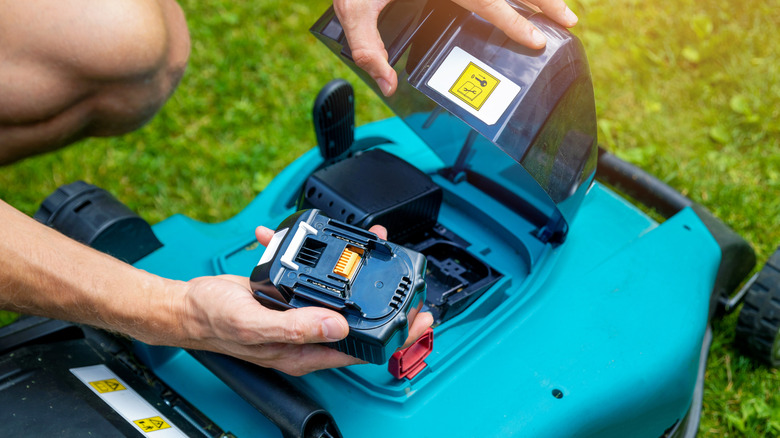 Person placing a battery into a blue battery-powered lawn mower
