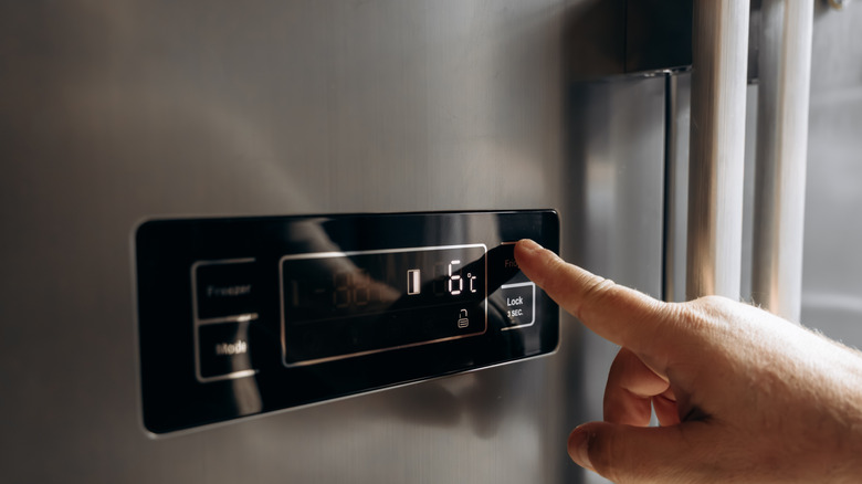Person pressing the digital panel on a modern fridge