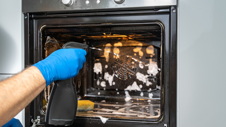 Gloved man washing oven 