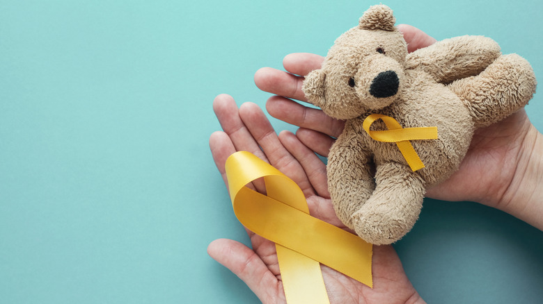 Person holding gold ribbon and teddy bear for childhood cancer awareness