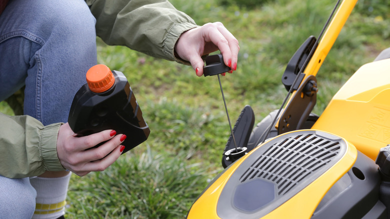 Pouring oil into lawn mower after checking oil level.