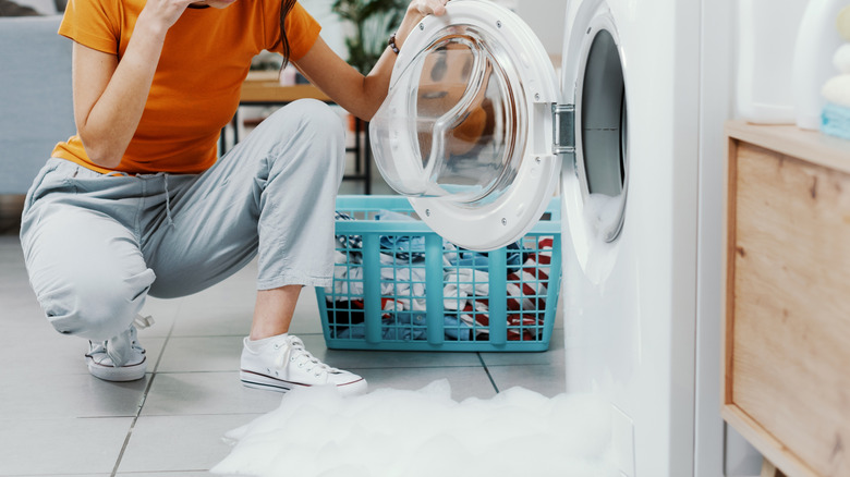 A woman on the phone crouching in front of a washer overloaded with suds