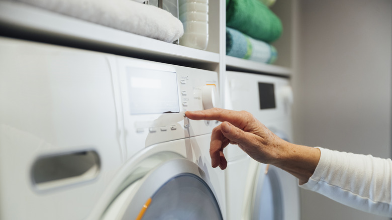 Hand pressing button on a white washing machine