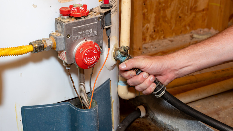 Person connecting a hose to a water heater for draining