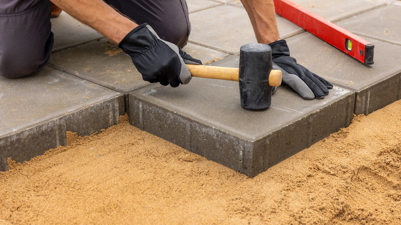 A person installing paving slabs with a rubber mallet