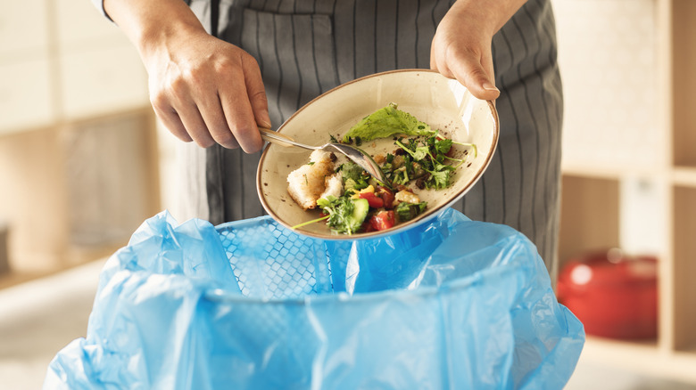 A woman scrapes leftover food into the trash.