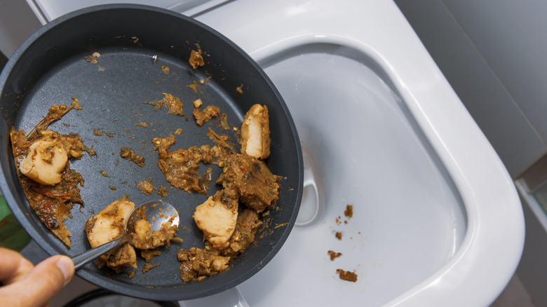 A hand dumps soiled meat from a pan into a toilet.