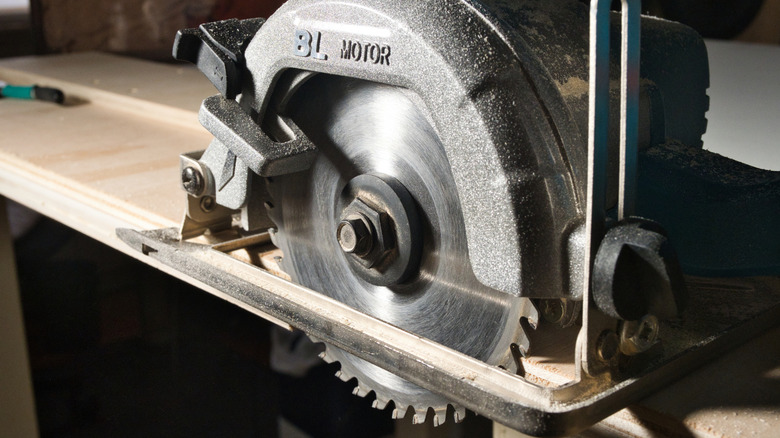 Close-up view of a power circular saw blade, teeth, and metal housing, covered in sawdust.