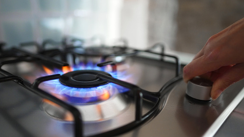 a person holding the knob of the gas burner on a stove