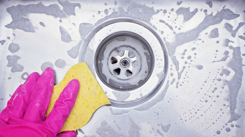 A person cleaning a metal sink with a sponge