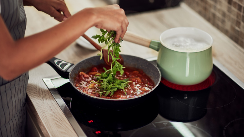 Woman cooking a meal on a stovetop with two sauce pans.