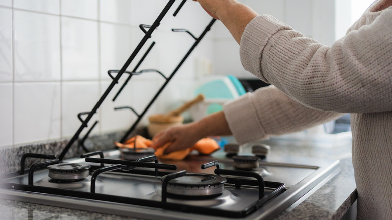 Woman cleaning a gas stovetop by lifting grate and wiping beneath.