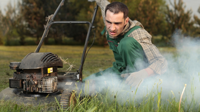 Man starting a lawn mower with an engine that's smoking