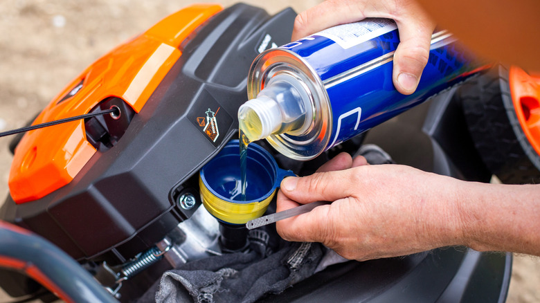 A person pouring oil into a lawn mower