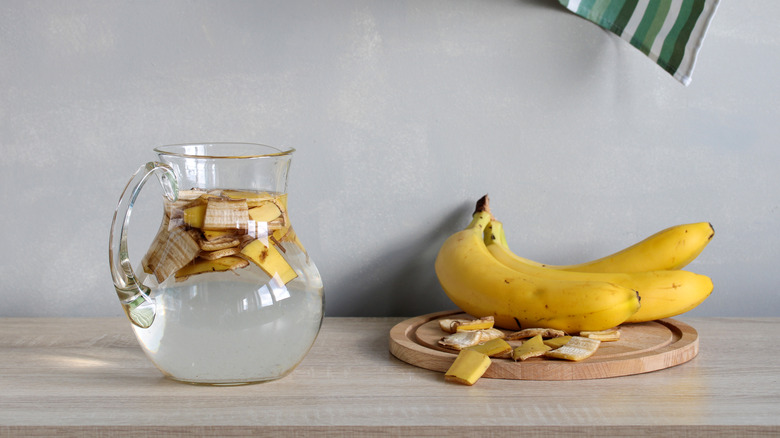 Bananas sitting next to a pitcher with water and pieces of banana peel