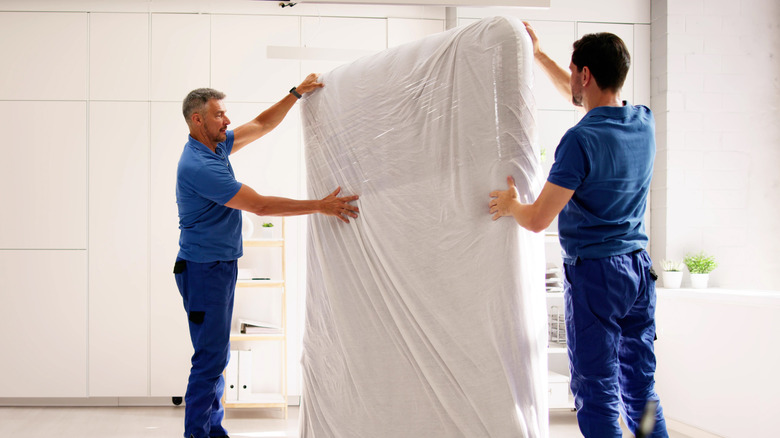 two delivery workers holding up mattress with protective cover on it