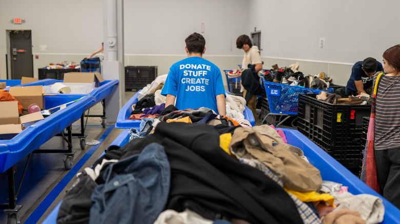 People shopping at the Goodwill outlet with donated items in bins showing a man in a blue shirt reading "donate stuff, create jobs"