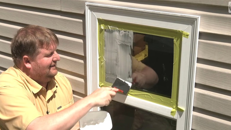 A smiling man applying white yogurt on a window pane