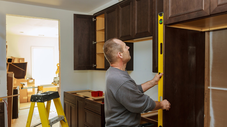 man measures cabinet with long level during a kitchen remodel