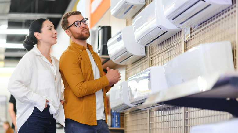 Two people look at air conditioners on the wall of a store