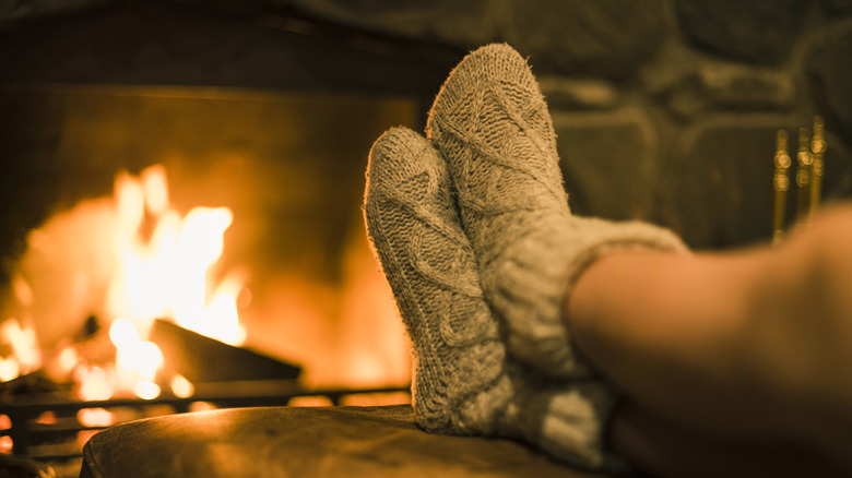Feet with knit socks sitting in front of a fireplace.