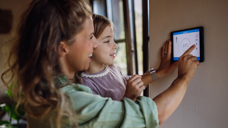 A woman and child setting temperatures on a modern, smart thermostat.