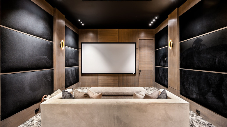 A dark, modern at-home movie room with large screen and chairs.