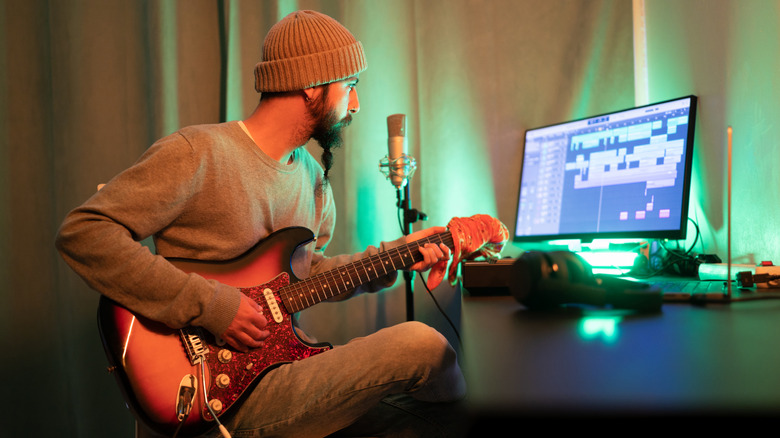 A man in a DIY recording studio with a guitar and recording equipment.