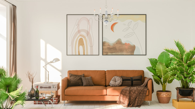 A living room with a terra cotta couch, plants, paintings, and a chandelier.