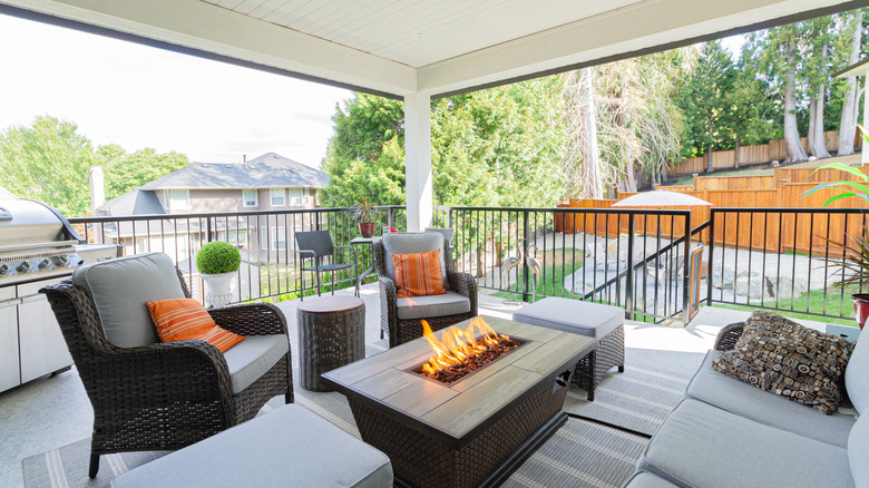 An outdoor, backyard deck with a fireplace, grill, and furniture.