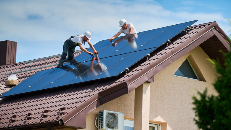 Construction workers installing solar panels on the roof of a house.