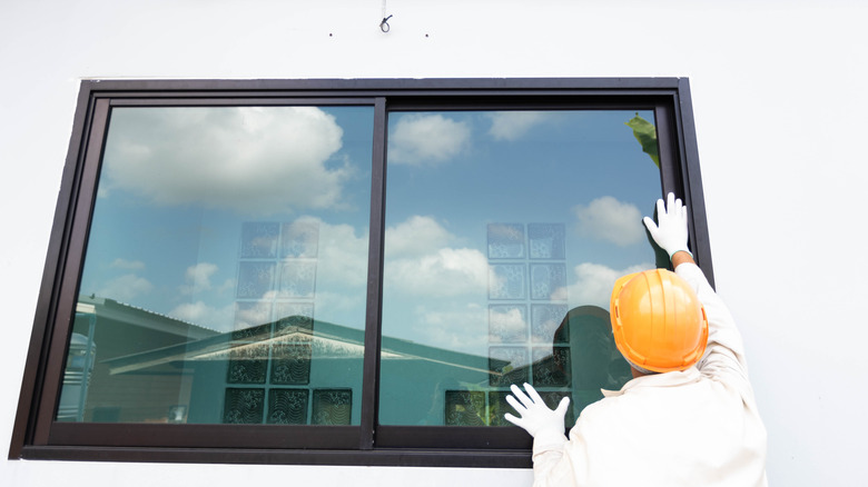 A man wearing a hardhat installing a new window frame.