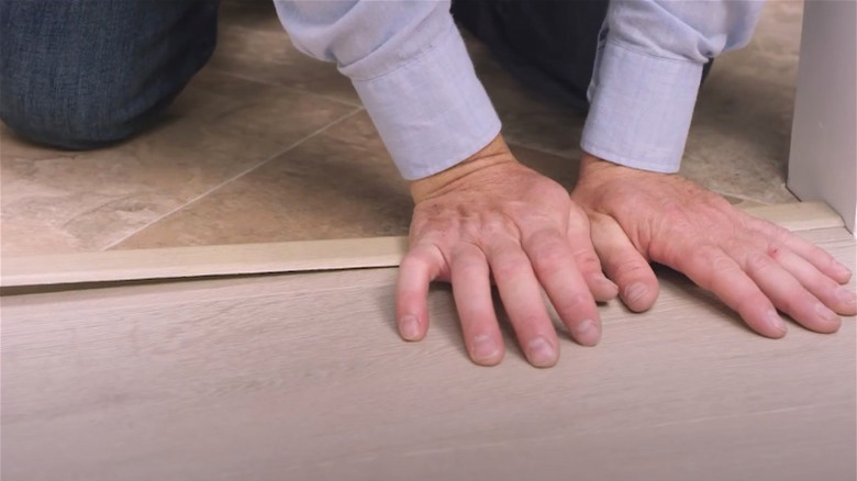 Person installing 4-in-1 transition strip between wood and tile floors