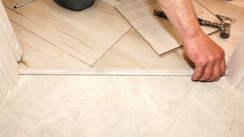 Mans hand installing a flooring transition strip