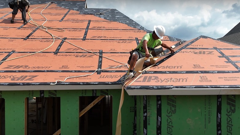 Two workers applying seal to the seams of a roof deck in a Fortified roof