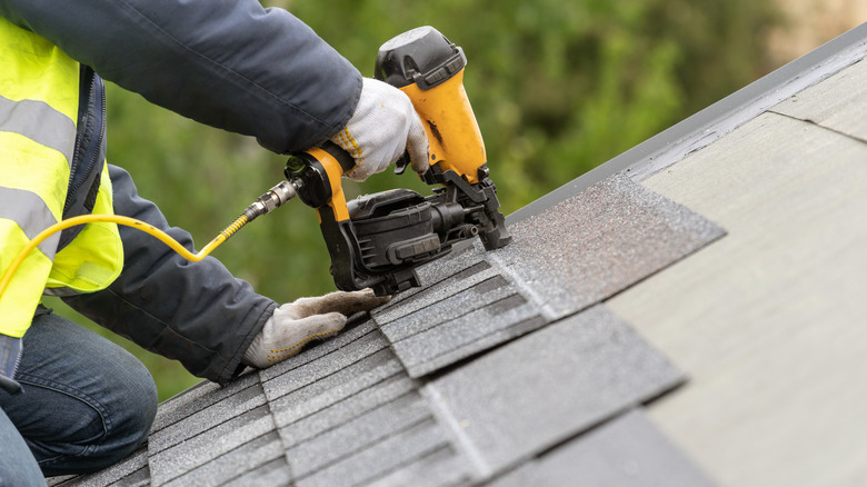 Worker wearing green high-visibility jacket fixing roof shingles