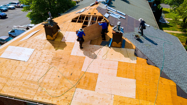 Three workers laying the roof deck and waterproof underlayment during roof construction