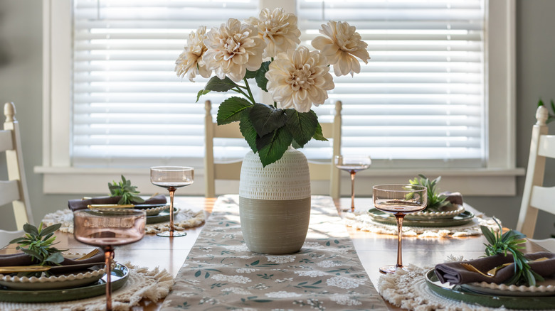 A dining table set with tableware and flowers for hosting a dinner party at home.
