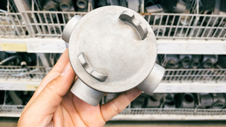 A person holds a round metal junction box with a cover