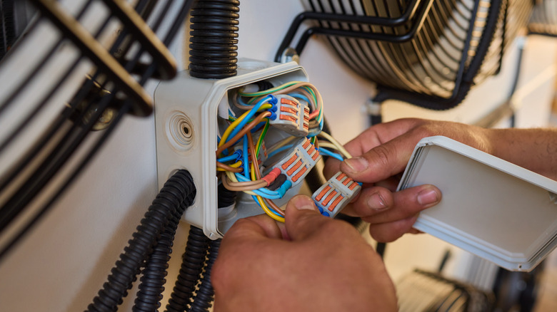 A pair of hands is shown holding colorful wires in a junction box