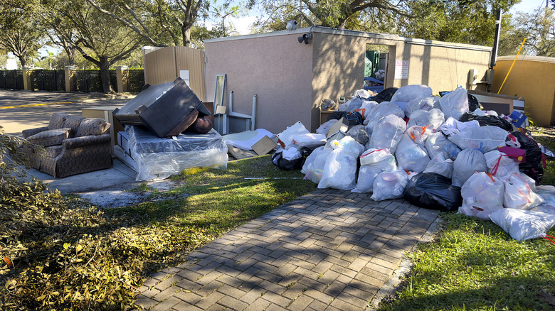 Piles of white trashbags and large pieces of furniture outside of a residential gate.