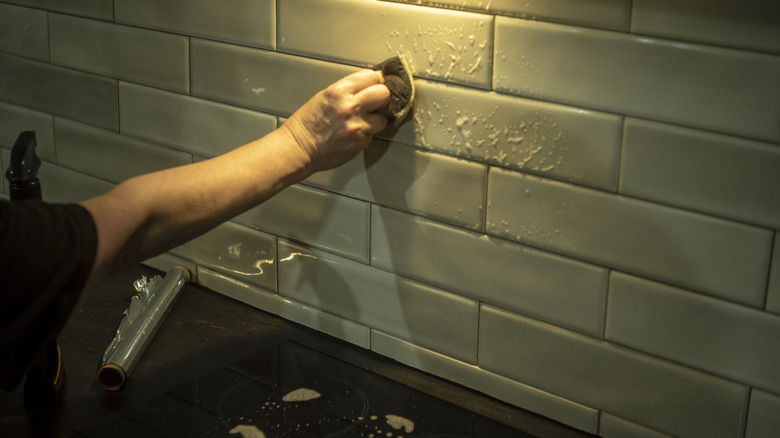 Person installing tile backsplash behind stove