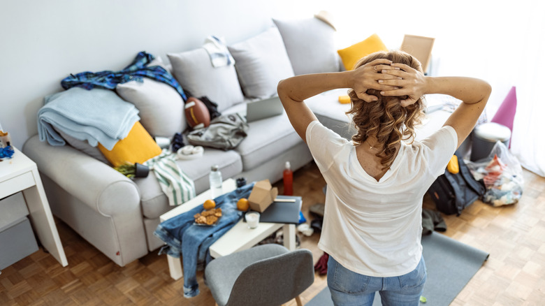 Person pictured from behind with hands on their head, looking at messy living room