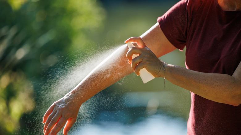 Person in red shirt applying mosquito spray outdoors