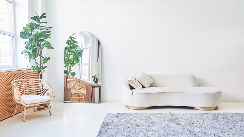 white room with white sofa, rattan chair, mirror, and plant