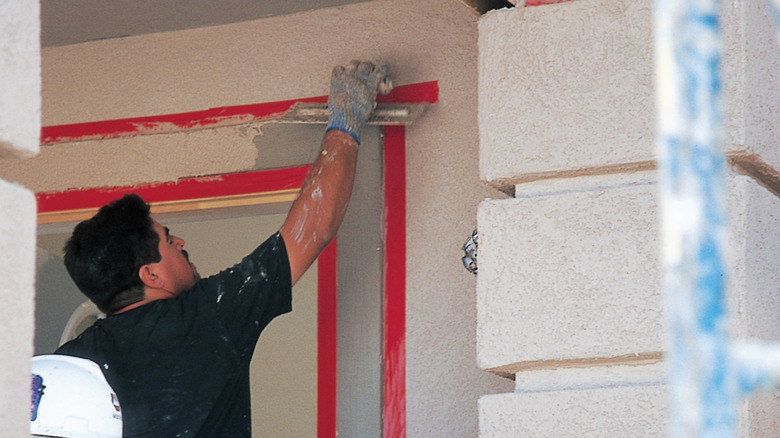 Person wearing gloves and applying stucco around red stucco tape
