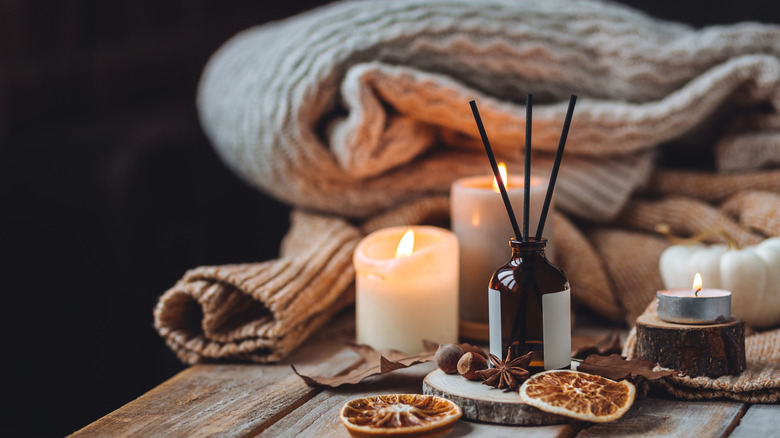 Candles, a scent diffuser, and a cozy folded blanket are on hand in a relaxing room.